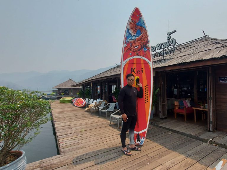 Pom stands with paddle board outside lakeside cafe