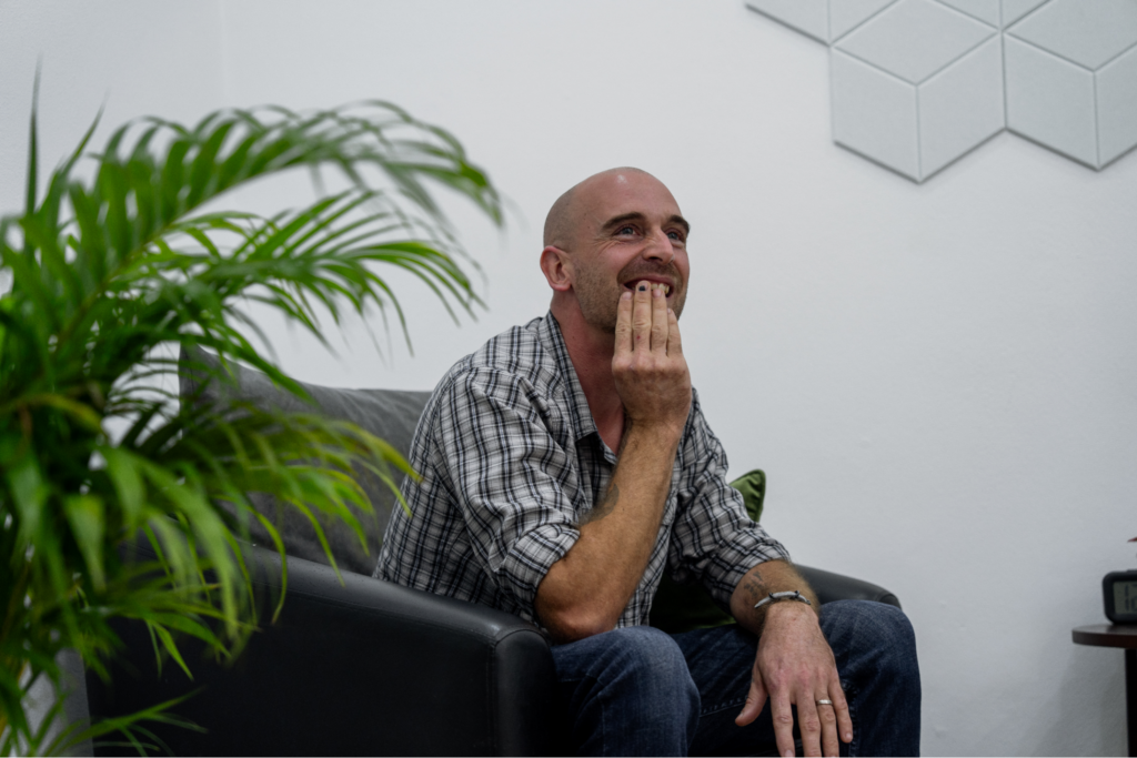 A male client is seated comfortably during a one-to-one therapy conversation in a quiet, minimalist room at One Step Rehab.