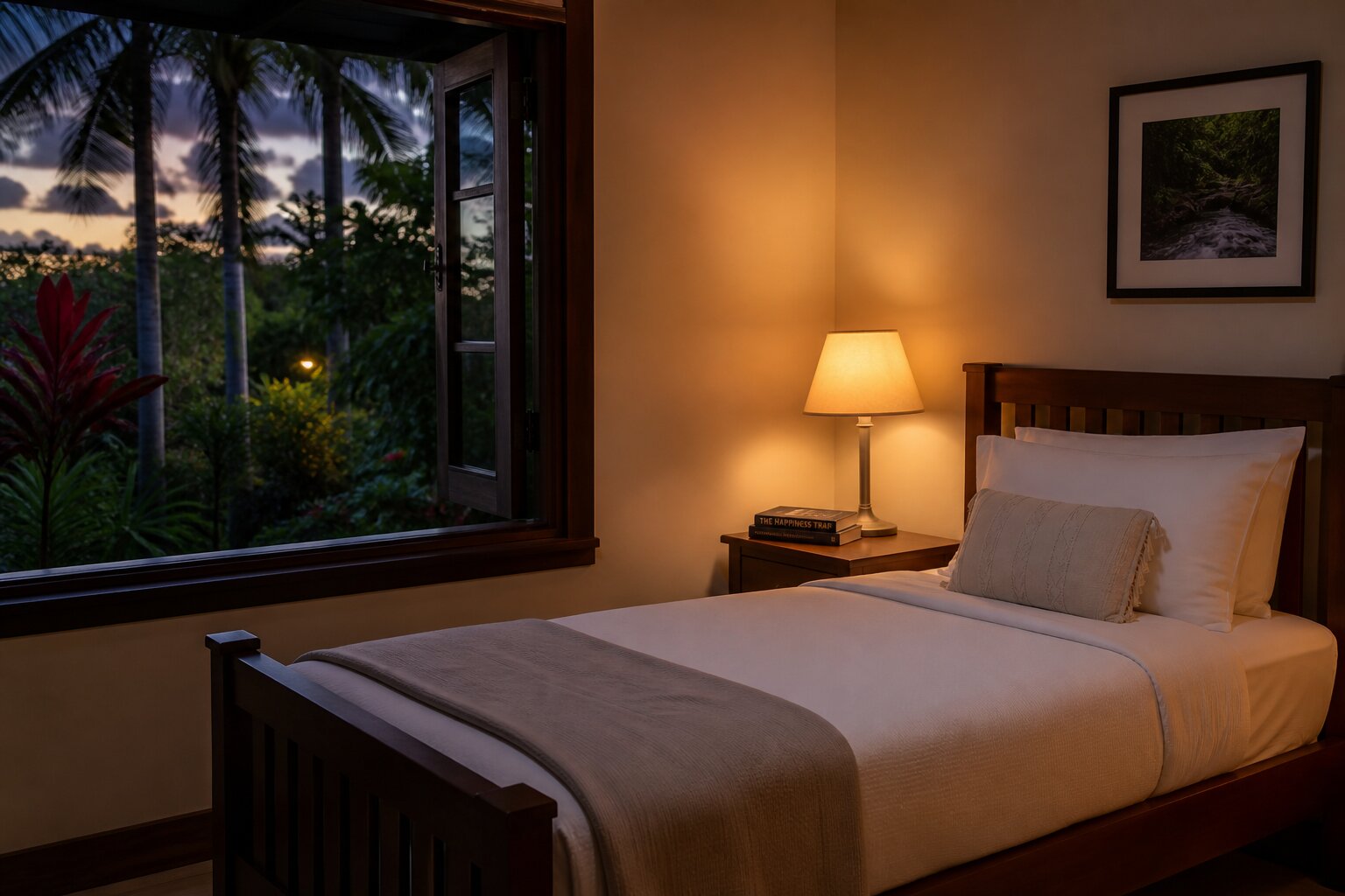 Clean comfortable bedroom with warm lamp light a book on the nightstand and tropical garden view at dusk